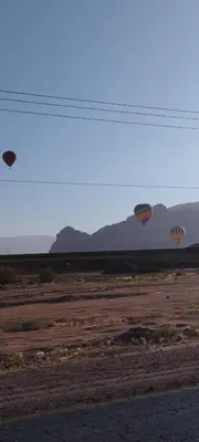 two hot air balloons flying over a dirt field at Wadi rum safari 1 camp in Wadi Rum