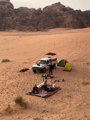 a group of people sitting in the desert with a car and a tent at Bedouin experiences in Aqaba