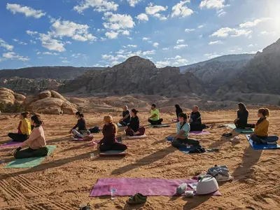a group of people sitting in the desert doing yoga at Namla Bedouin Camp in Umm Şawwānah