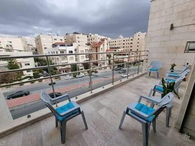 a balcony with three chairs and a view of a city at Deir Ghbar 3 rooms apart in Amman