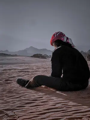 a person sitting on the sand on the beach at Whispering Rum in Wadi Rum