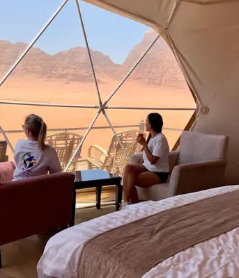 two women sitting in a tent looking out at the desert at Hakon Matata Wadi Rum Jeep Tours Camp in Wadi Rum