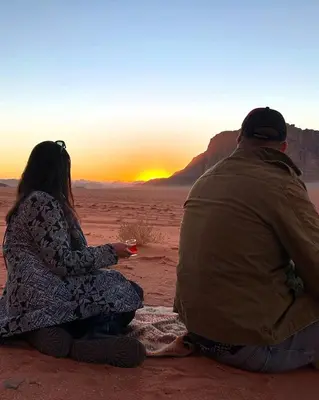 a man and woman sitting in the desert watching the sunset at Wadi Rum The ARC camp in Wadi Rum