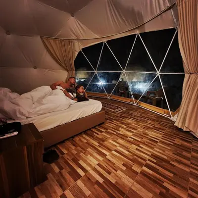 a man and a baby laying on a bed in a tent at Wadi Rum Calma camp in Aqaba