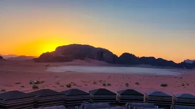 a sunset over a desert with tents and a mountain at Wadi Rum Majestic Camp in Wadi Rum