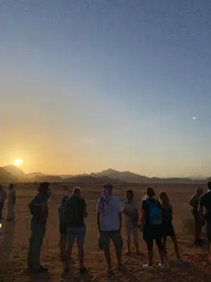 a group of people standing in the desert watching the sunset at Bedouin Secret Camp in Wadi Rum