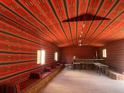 a room with a red wall with a table and chairs at Desert Gate Camp in Wadi Rum