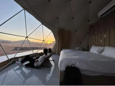 two people sitting in a room with a bed and a window at camp scylla Wadi Rum in Wadi Rum